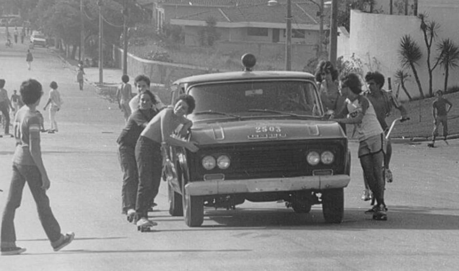 Meninos andando de skate acompanhados pela Polícia na rua em 1975, em uma cena de infância e segurança pública no Brasil.